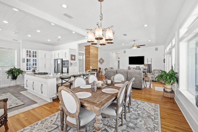 dining space with ceiling fan with notable chandelier, light hardwood / wood-style floors, and beamed ceiling