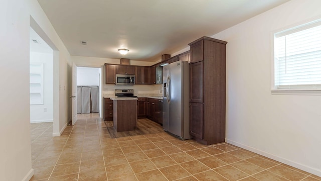 kitchen featuring dark brown cabinetry, light tile flooring, a center island, and stainless steel appliances