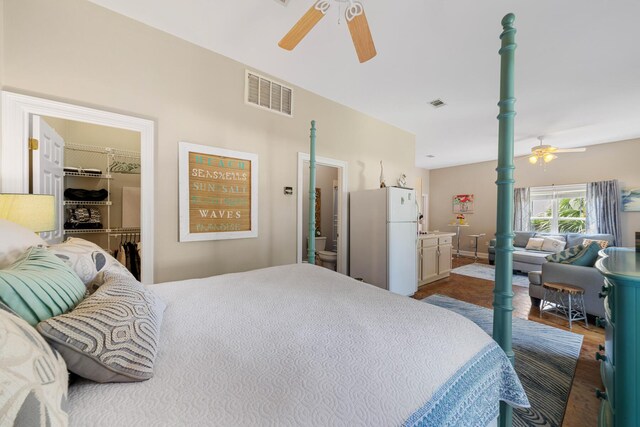 bedroom with a walk in closet, white fridge, a closet, ensuite bathroom, and ceiling fan