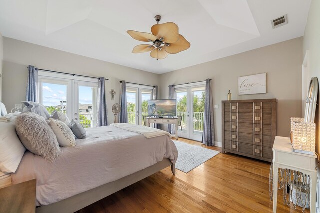 bedroom featuring wood-type flooring, a tray ceiling, french doors, access to outside, and ceiling fan