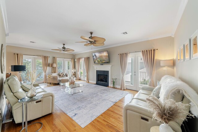 living room featuring a fireplace, crown molding, french doors, light hardwood / wood-style flooring, and ceiling fan