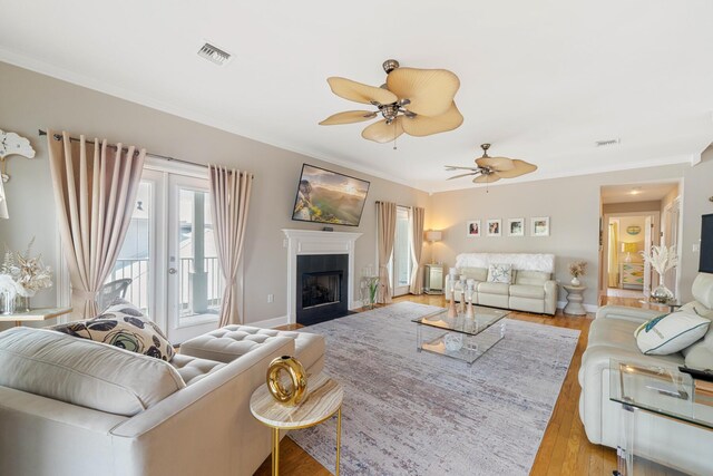 living room with a tiled fireplace, crown molding, light hardwood / wood-style flooring, and ceiling fan