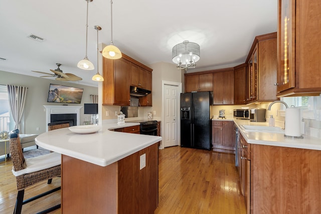 kitchen with light hardwood / wood-style flooring, ceiling fan with notable chandelier, sink, black appliances, and pendant lighting