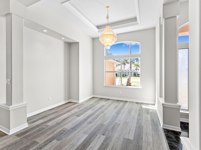 unfurnished dining area with a raised ceiling, decorative columns, a notable chandelier, and hardwood / wood-style floors