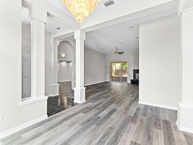 unfurnished living room featuring ceiling fan with notable chandelier, decorative columns, and hardwood / wood-style floors