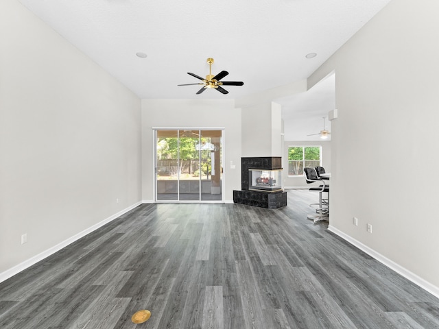 unfurnished living room featuring a multi sided fireplace, dark wood-type flooring, and ceiling fan