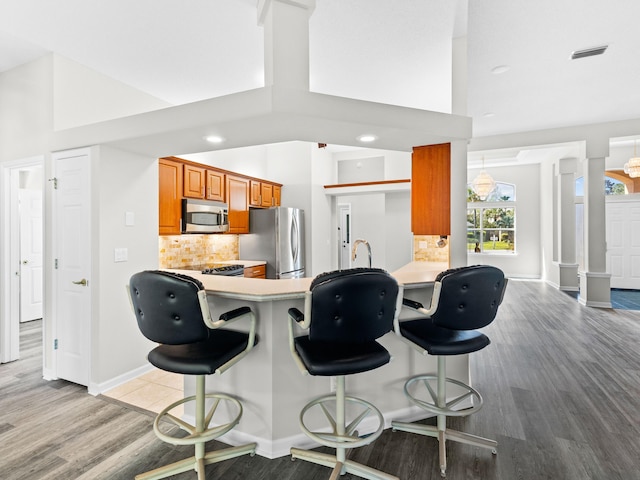 kitchen with decorative columns, kitchen peninsula, a breakfast bar, backsplash, and appliances with stainless steel finishes