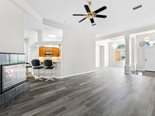 living room with a fireplace, ceiling fan, dark hardwood / wood-style flooring, and decorative columns