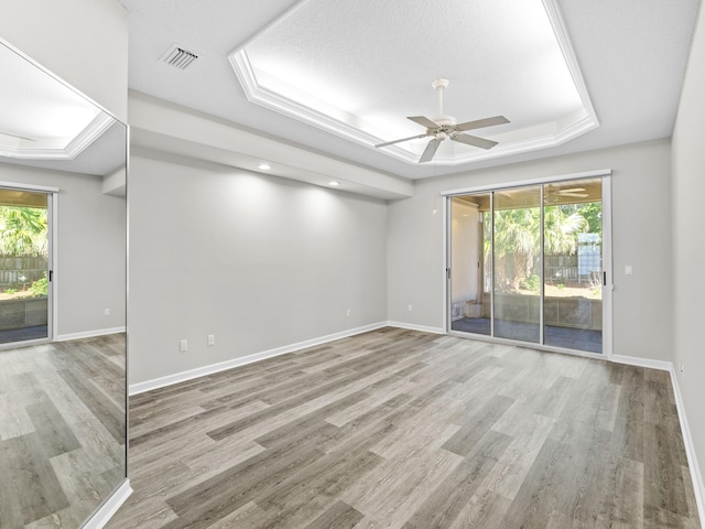 empty room with a tray ceiling, light hardwood / wood-style flooring, and ceiling fan