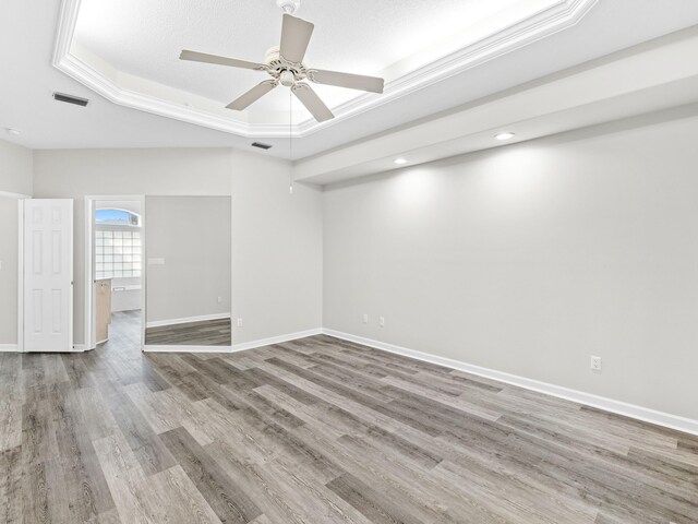 spare room with ceiling fan, light hardwood / wood-style flooring, a tray ceiling, and ornamental molding