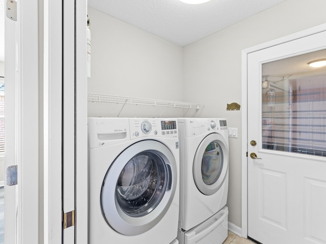 clothes washing area featuring light tile patterned flooring, washer and dryer, and a textured ceiling