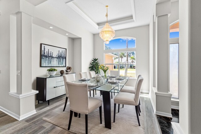 dining space with a tray ceiling, a notable chandelier, hardwood / wood-style floors, and ornate columns