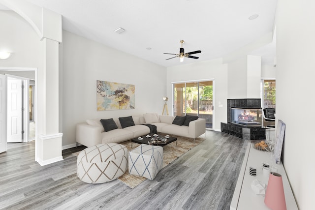 living room with ceiling fan, a tiled fireplace, light hardwood / wood-style flooring, and ornate columns