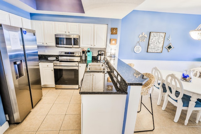 kitchen featuring appliances with stainless steel finishes, light tile floors, sink, white cabinetry, and dark stone counters