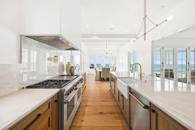 kitchen featuring appliances with stainless steel finishes, backsplash, hanging light fixtures, a chandelier, and light hardwood / wood-style flooring