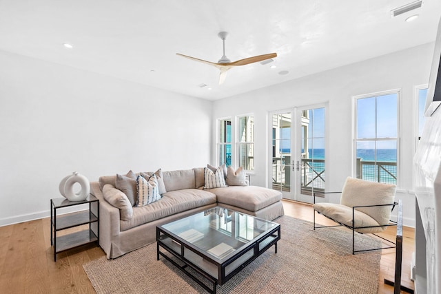 living room featuring french doors, light hardwood / wood-style floors, a water view, and ceiling fan