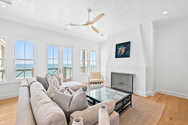 living room featuring a water view, ceiling fan, light wood-type flooring, and a large fireplace