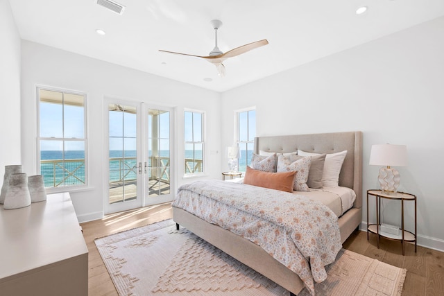 bedroom with ceiling fan, a water view, access to exterior, wood-type flooring, and french doors