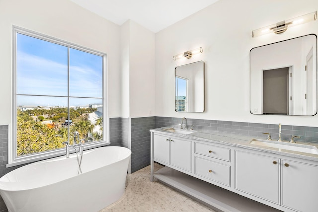 bathroom with vanity with extensive cabinet space, tile walls, backsplash, a bathing tub, and dual sinks