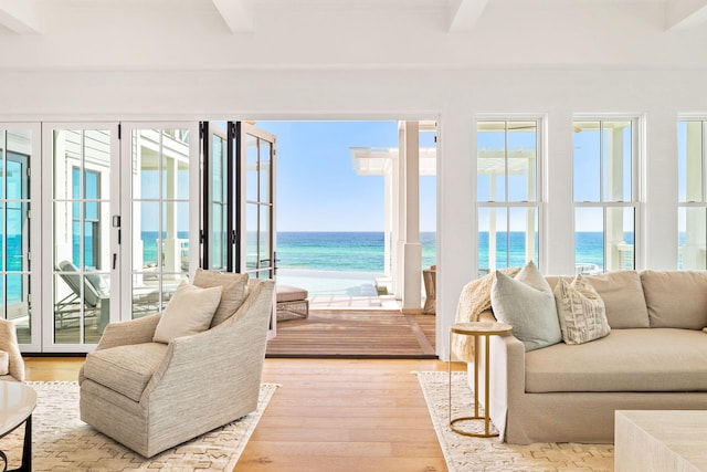 living room with light hardwood / wood-style flooring, beamed ceiling, and a water view