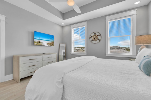 bedroom featuring multiple windows, ceiling fan, a raised ceiling, and light wood-type flooring