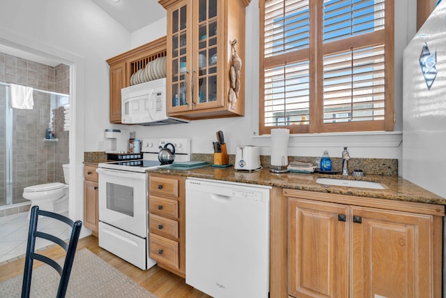 kitchen with sink, white appliances, dark stone countertops, and light hardwood / wood-style floors