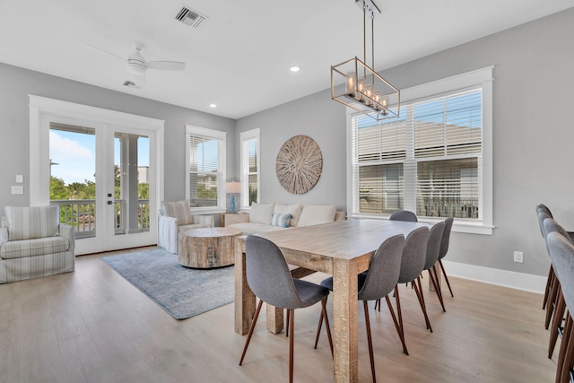 dining space featuring ceiling fan with notable chandelier, a wealth of natural light, french doors, and light wood-type flooring