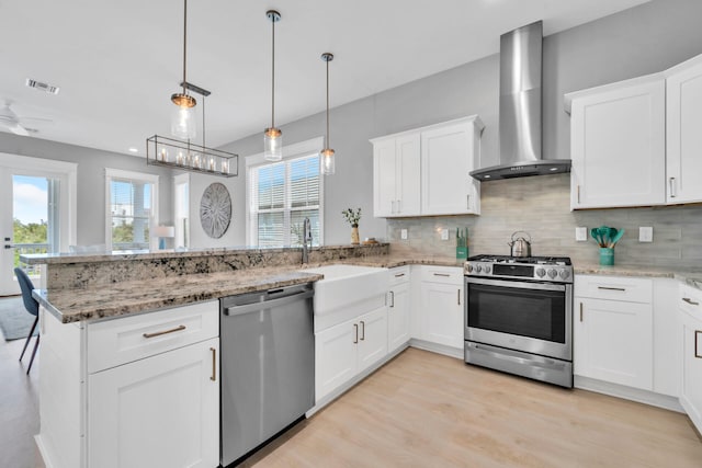 kitchen featuring hanging light fixtures, light hardwood / wood-style flooring, wall chimney range hood, and stainless steel appliances