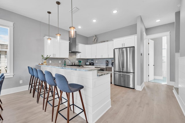 kitchen featuring light hardwood / wood-style floors, stainless steel refrigerator, wall chimney exhaust hood, white cabinetry, and pendant lighting