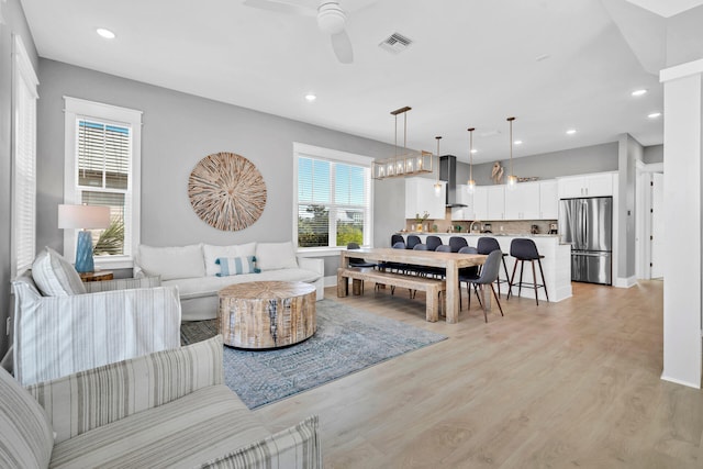 living room with ceiling fan with notable chandelier, light hardwood / wood-style floors, and a wealth of natural light