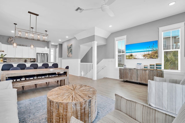 living room featuring light hardwood / wood-style floors, a healthy amount of sunlight, and ceiling fan with notable chandelier