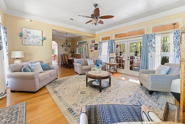 living room featuring ceiling fan with notable chandelier, french doors, light hardwood / wood-style floors, and crown molding