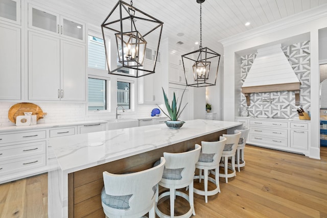 kitchen featuring a kitchen island, tasteful backsplash, white cabinetry, decorative light fixtures, and light hardwood / wood-style flooring