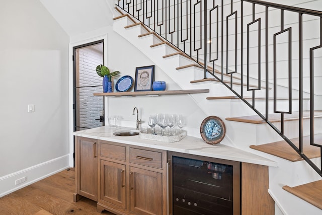 bar with beverage cooler, sink, vaulted ceiling, hardwood / wood-style flooring, and light stone countertops