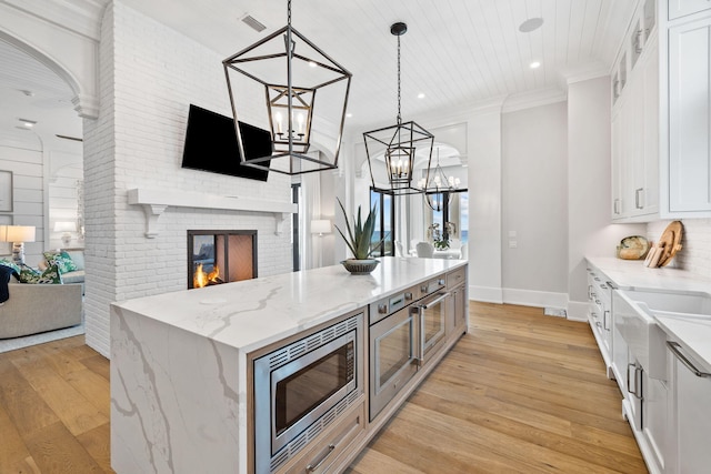 kitchen featuring a fireplace, white cabinets, a notable chandelier, light hardwood / wood-style floors, and stainless steel microwave