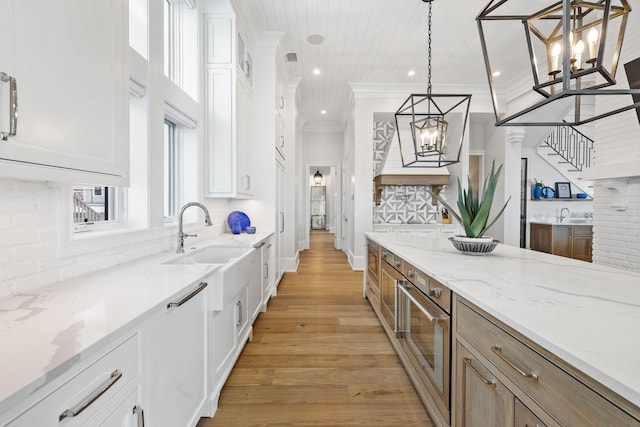 kitchen featuring decorative light fixtures, light stone countertops, crown molding, white cabinetry, and light hardwood / wood-style floors