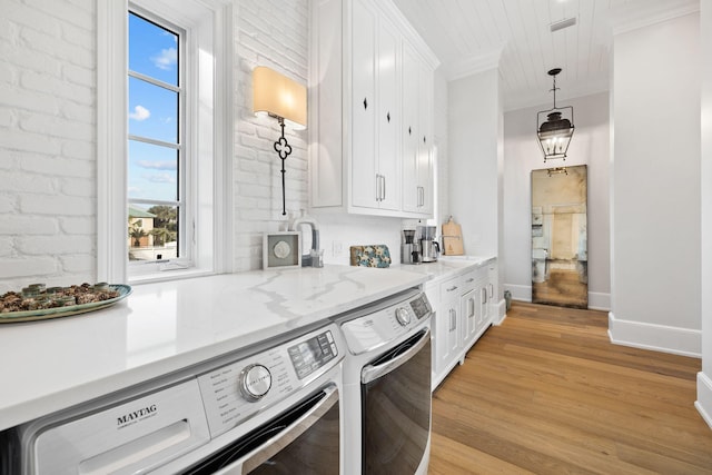 kitchen with white cabinets, light wood-type flooring, hanging light fixtures, brick wall, and independent washer and dryer