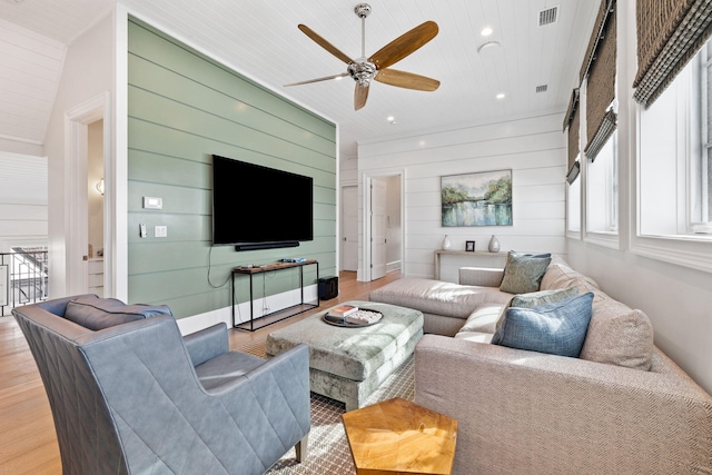 living room featuring light hardwood / wood-style flooring, ceiling fan, and wooden walls