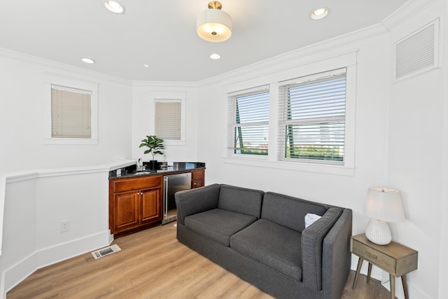 living room with beverage cooler, crown molding, and light wood-type flooring