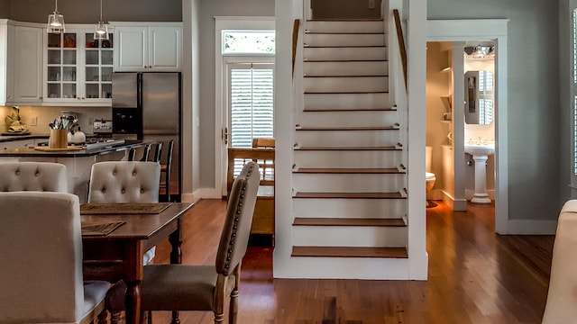 interior space featuring white cabinetry, dark wood-type flooring, tasteful backsplash, stainless steel fridge, and decorative light fixtures