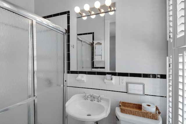 bathroom featuring toilet, a shower with shower door, sink, and tile walls