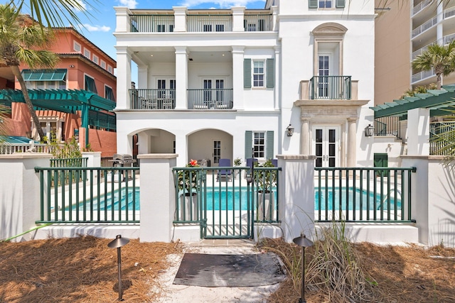 view of front of property featuring a patio area, fence, a balcony, and an outdoor pool