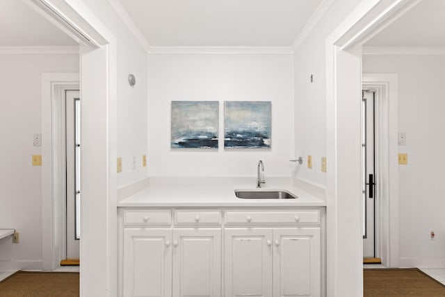 kitchen featuring white cabinets, ornamental molding, light countertops, and a sink