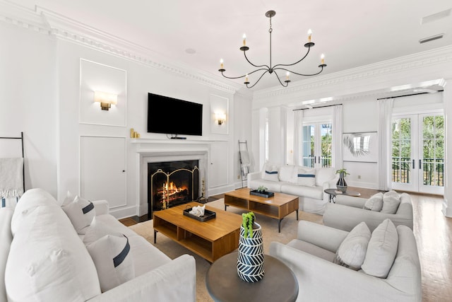 living room with wood finished floors, a fireplace with flush hearth, french doors, ornamental molding, and decorative columns