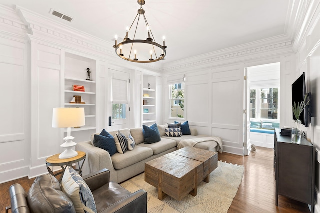 living room with a notable chandelier, a decorative wall, wood finished floors, visible vents, and built in features