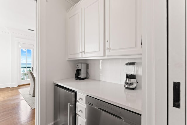 bar with light hardwood / wood-style flooring, white cabinetry, ornamental molding, stainless steel dishwasher, and tasteful backsplash