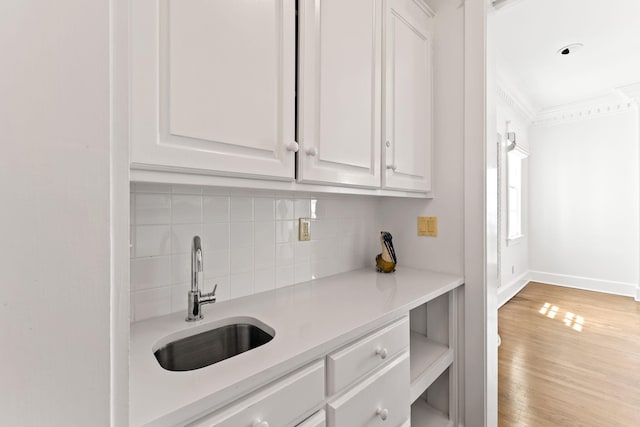 kitchen featuring light countertops, backsplash, white cabinets, a sink, and wood finished floors