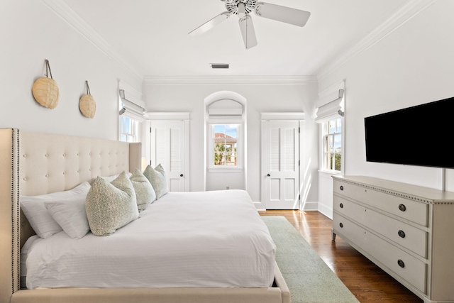 bedroom with multiple closets, visible vents, ornamental molding, ceiling fan, and wood finished floors