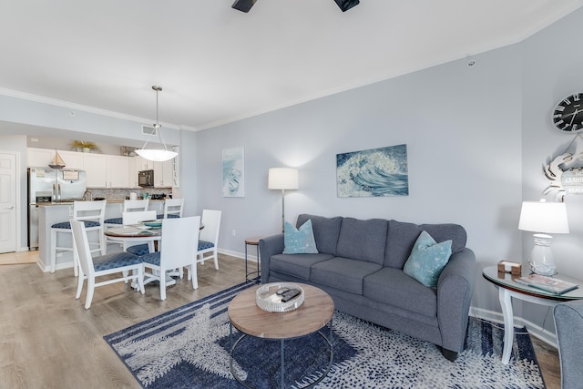 living area with crown molding, light wood-type flooring, and baseboards