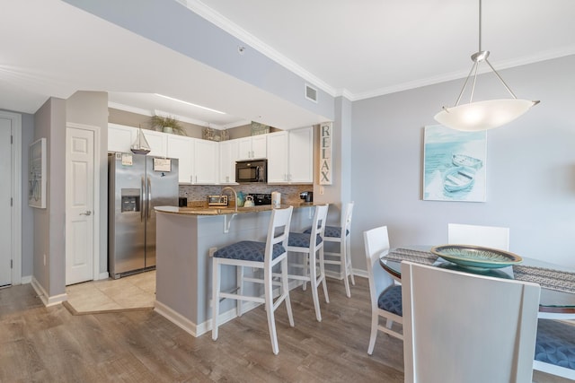 kitchen with stainless steel fridge, white cabinets, a peninsula, hanging light fixtures, and black microwave